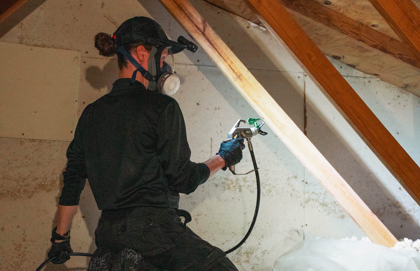 Taps Pest Services technician in a respirator spraying drywood termite treatment across attic framing at a Riverview, FL home