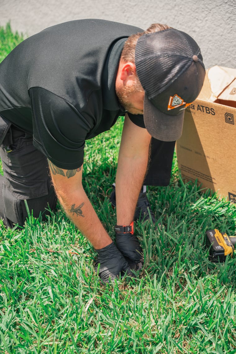 Taps Pest Services technician installing a Trelona ATBS termite bait station at a commercial property in Riverview, FL